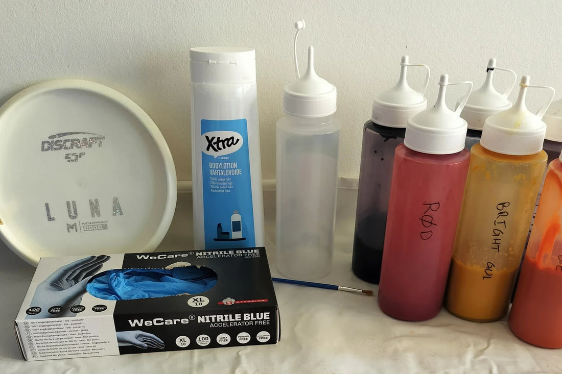 Utstyr til disc dye: en hvit disc, flasker med farge, hansker og en pensel