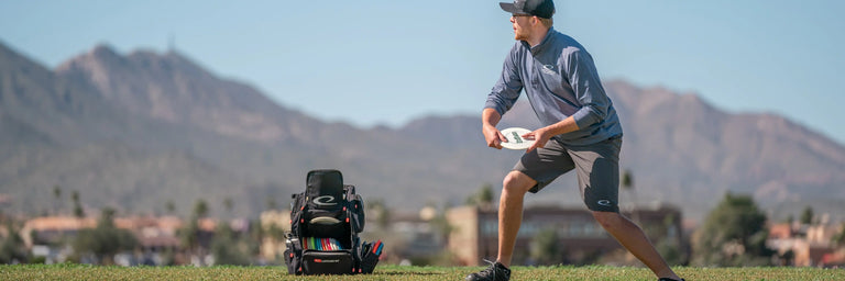 Disc golfer der gør klar til at kaste sin driver foran sin taske med en bjerkæde i baggrunden