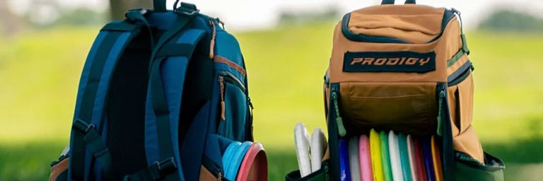 To disc golf tasker fra Prodigy i forskellige farver med en slørret baggrund af et bakket landskab