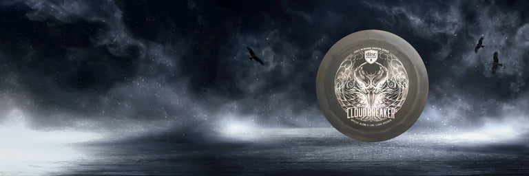 En grå Cloudbreaker disc golf disc fra Discmania klippet ind på en mørk himmel med ravne der flyver omkring
