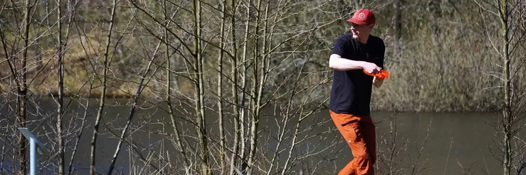 Disc golfer i sort T-shirt der gør klar til at kaste sin driver med en sø i baggrunden