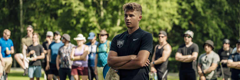 Discgolfspiller venter med tilskuere i baggrunden