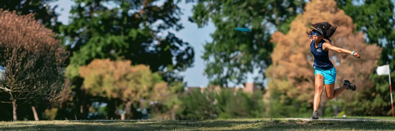 Kvindelig disc golf spiller sponsoreret af Trilogy der er midt i et langt baghåndskast.